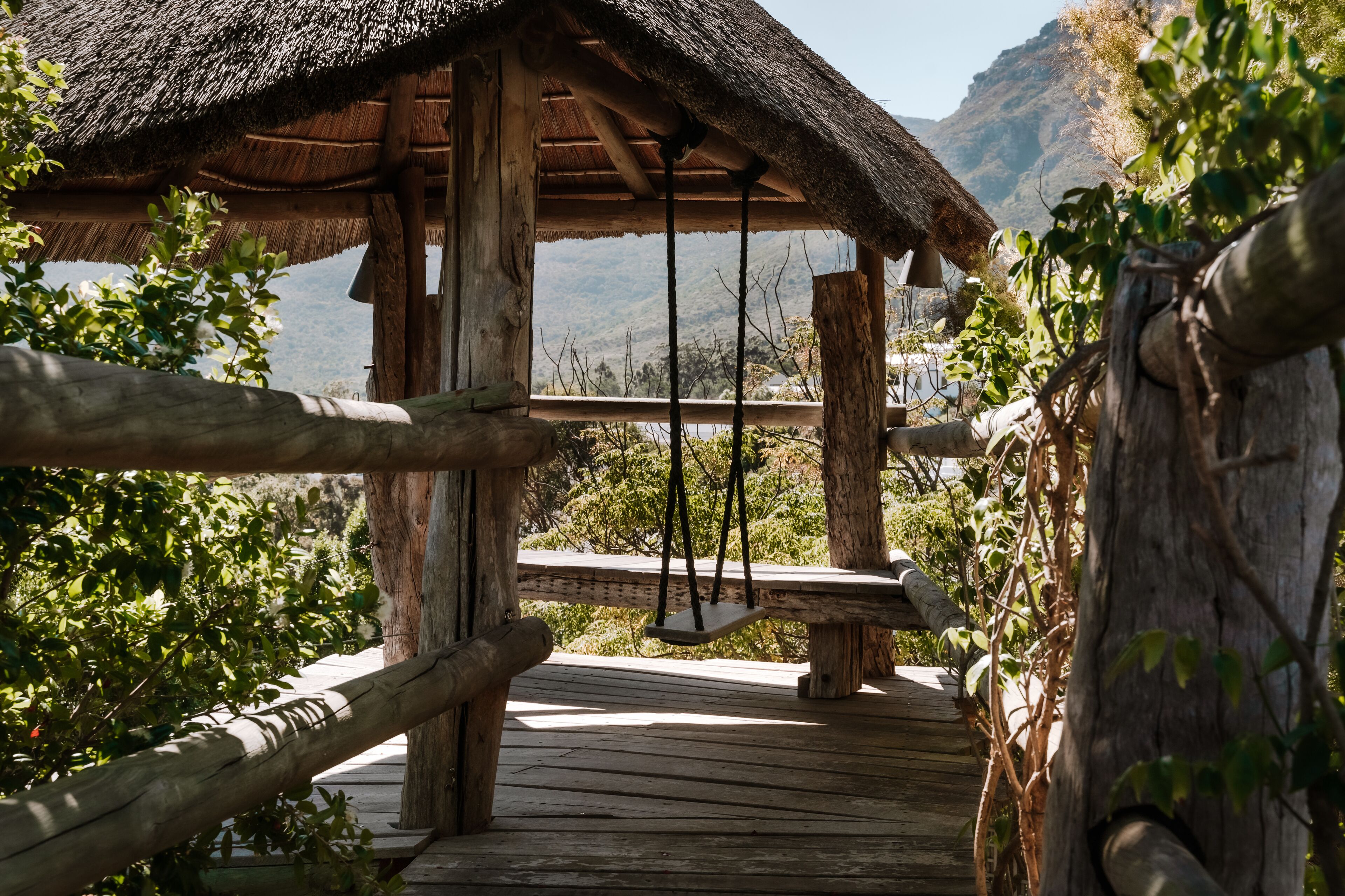 A wooden structure with a thatched roof, a swing, and a view of a mountainous landscape.