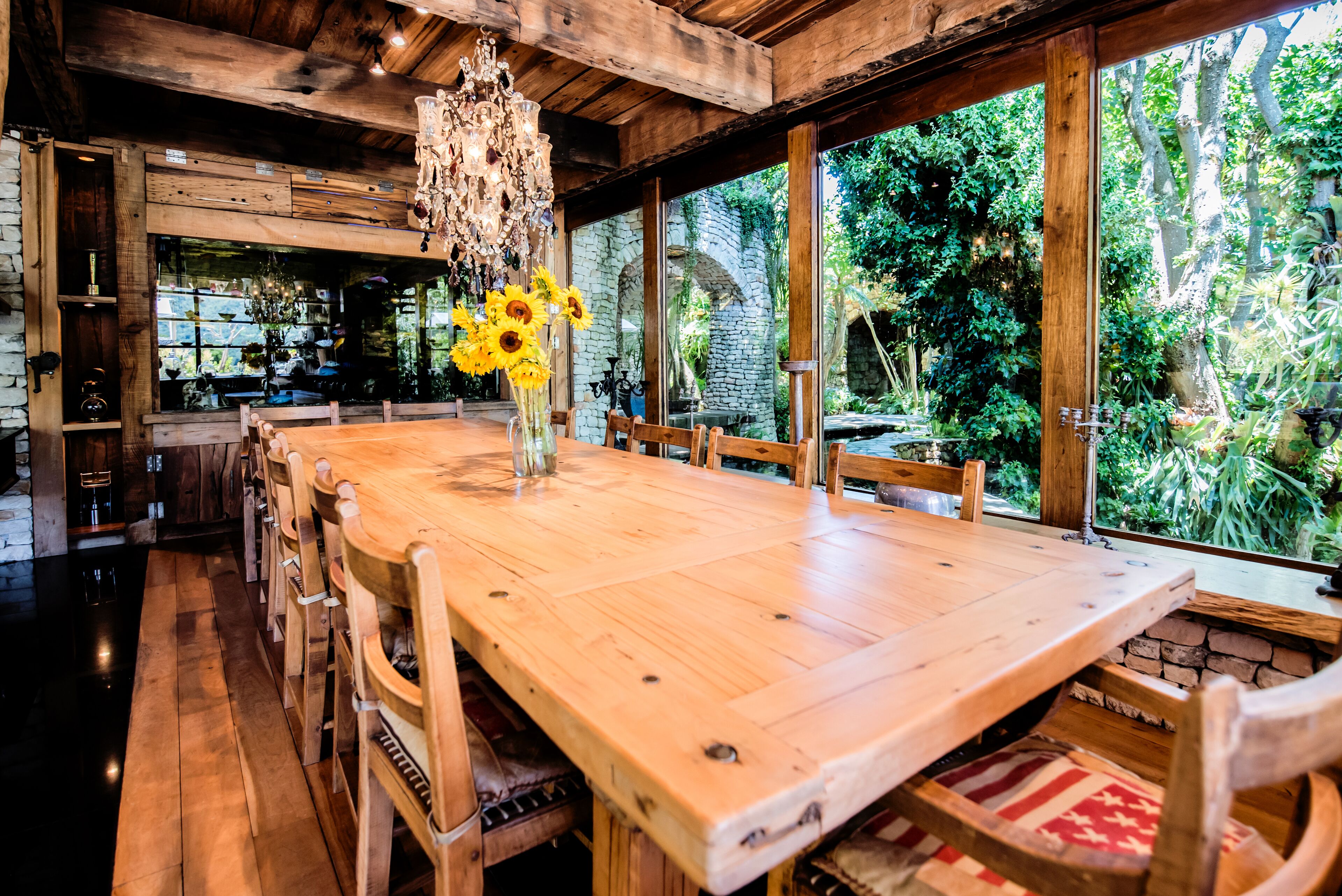 Une table à manger en bois, des chaises, un lustre et un vase rempli de tournesols.