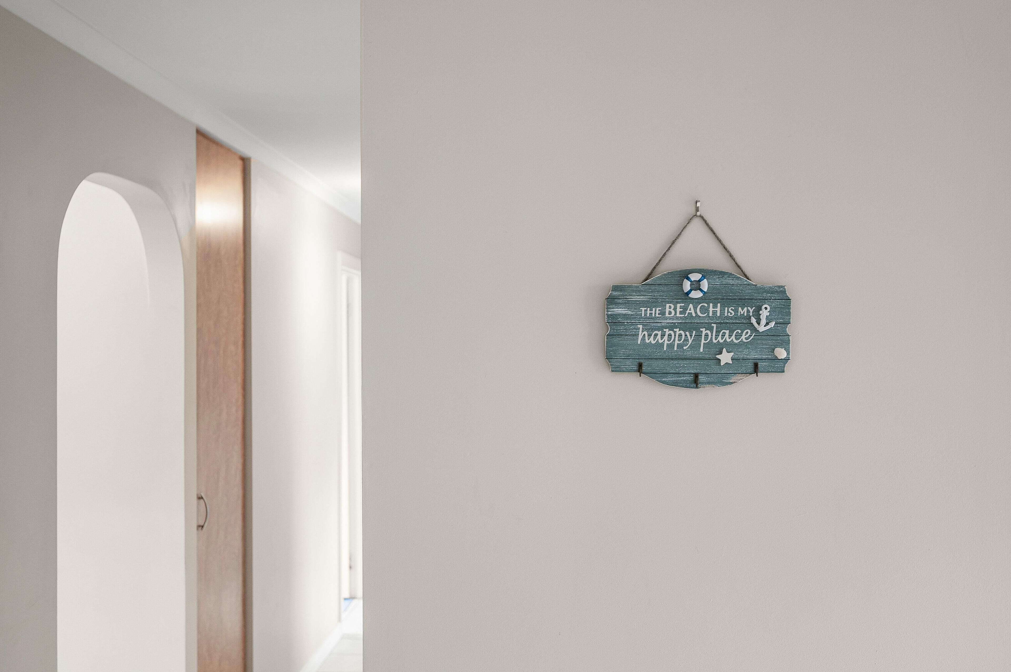 Een hal met een houten deur en een bord aan de muur waarop staat: THE BEACH IS MY happy place.