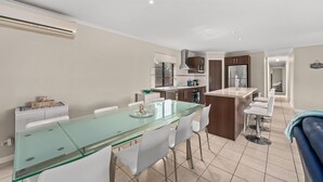 A modern kitchen with a glass dining table, white chairs, and a blue sofa. - Seacret Oasis - Aldinga Beach - C21 SouthCoast Holidays (Aldinga Beach)