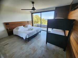 Un dormitorio con una cama, una mesita de noche, un ventilador de techo y una ventana con vistas.