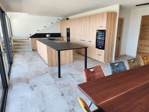 A modern kitchen with a central island, wooden cabinets, and a staircase leading to an upper level.