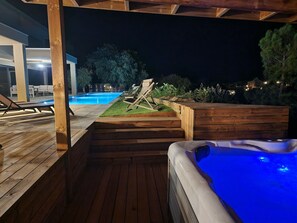 Eine Holzterrasse mit Whirlpool, Pool und Liegestühlen.