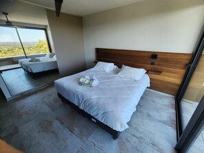 Une chambre à coucher moderne avec un grand lit, une tête de lit en bois et une vue sur l’extérieur.