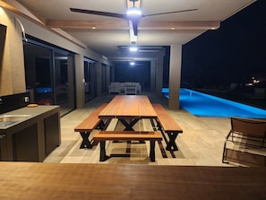 Un espace repas extérieur moderne, doté d’une piscine, d’un ventilateur de plafond et d’un coin cuisine.