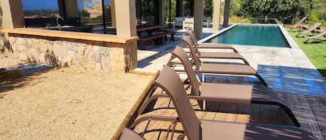 A poolside area with lounge chairs, a stone wall, and a view of the landscape.