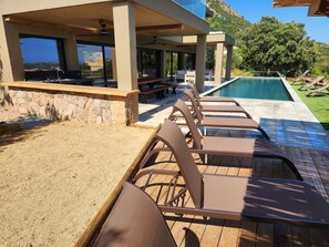 A poolside area with lounge chairs, a stone wall, and a view of the landscape. - Villa Aria Terra — Pinarello, sea view, heated pool 29°C, sea-view sauna (Conca)
