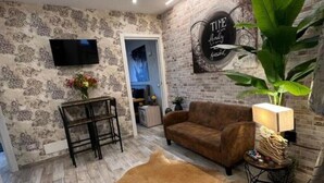 A living room with patterned wallpaper, a brown sofa, a leather rug, a TV mounted on the wall, and a decorative sign.