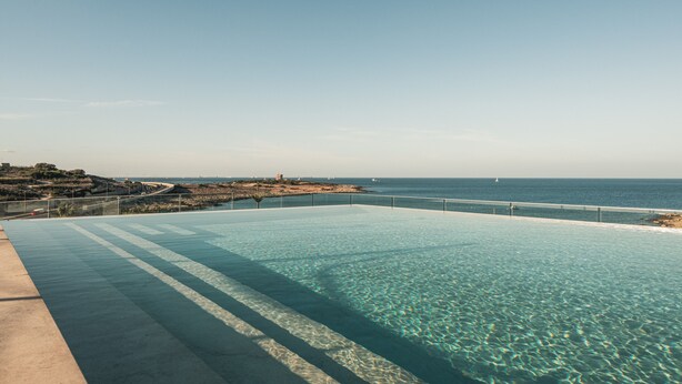 A clear blue infinity pool with a view of the sea and a distant shoreline.