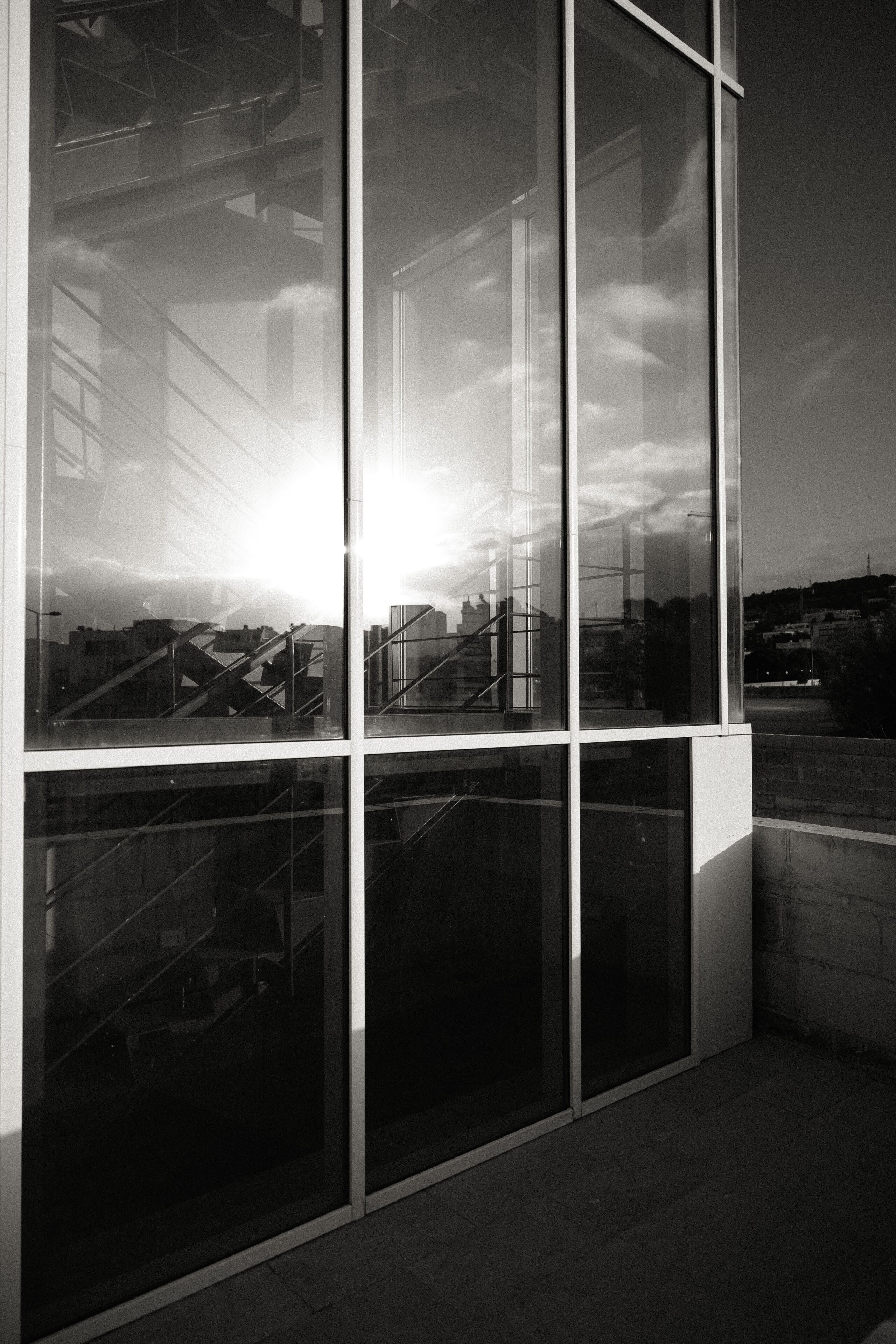 Ein modernes Gebäude mit großen Glasfenstern, die einen Stadtblick reflektieren, und einer Treppe.