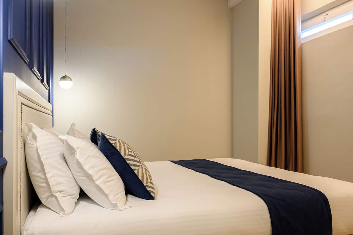 A neatly made bed with a headboard, a small round table, and a hanging light fixture.