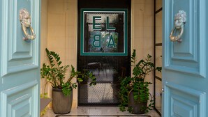 A hallway with a marble floor, a neon sign reading "ELBA," and two potted plants.