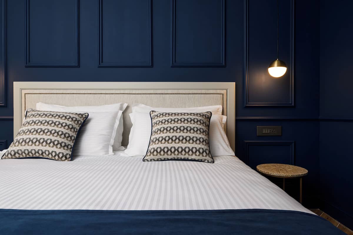 A neatly made bed with patterned pillows, a round side table, and a wall-mounted light fixture.