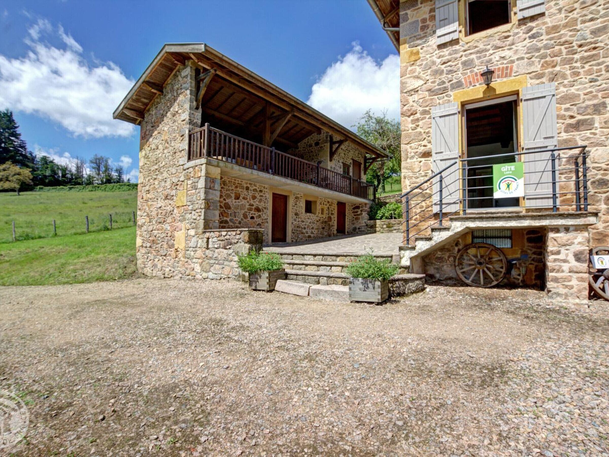 A stone building with a wooden balcony and a sign indicating a gîte location.