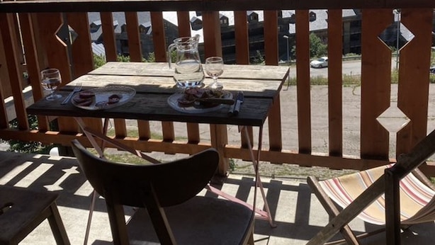A wooden table with plates of food and glasses, a chair, and a hammock on a balcony with a view of a lake and hills. - 3-Room Duplex - Lake and Mountain View - Parking Included (Les Angles)