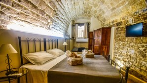 A narrow, stone-walled room with a bed, a TV, and a window. - Domum in petra, the house in the rock. A short walk from the historic center of Modica (Modica)