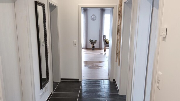 A hallway with dark tiled flooring, white walls, and doors on both sides. - Apartment "Waldblick" with Balcony & Wi-Fi (Westerheim)
