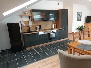 Een moderne keuken met een ingebouwde oven, een vaatwasser en een koffiezetapparaat. Er staat een eettafel met stoelen en een plant in de hoek.