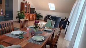 A dining area with a wooden table set for four, surrounded by chairs. There is a cabinet with glass doors, a television, and a window with curtains. - Apartment "Waldblick" with Balcony & Wi-Fi (Westerheim)