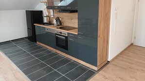 A modern kitchen with a black refrigerator, a built-in oven, a coffee maker, and a wooden countertop. - Apartment "Waldblick" with Balcony & Wi-Fi (Westerheim)