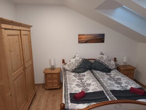 Een slaapkamer met een bed, twee nachtkastjes, een houten garderobe, een schilderij en een dakraam.