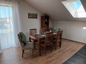 Een eetgedeelte met een houten tafel, stoelen, een boekenkast en uitzicht door een dakraam.