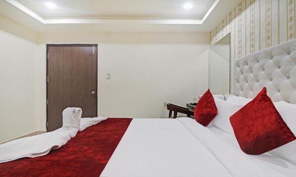 Una habitación de hotel con cama, alfombra roja, puerta de madera y cabecero blanco.