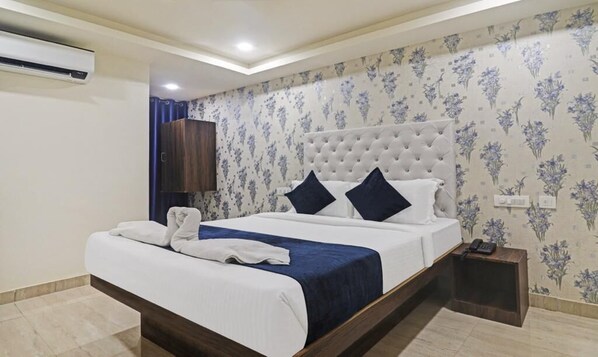 A neatly made bed with a white and blue bedspread, a wooden headboard, and a bedside table with a phone.