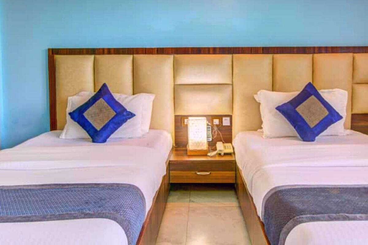 A hotel room with two beds, each with a headboard, a nightstand with a phone, and a wall-mounted light.