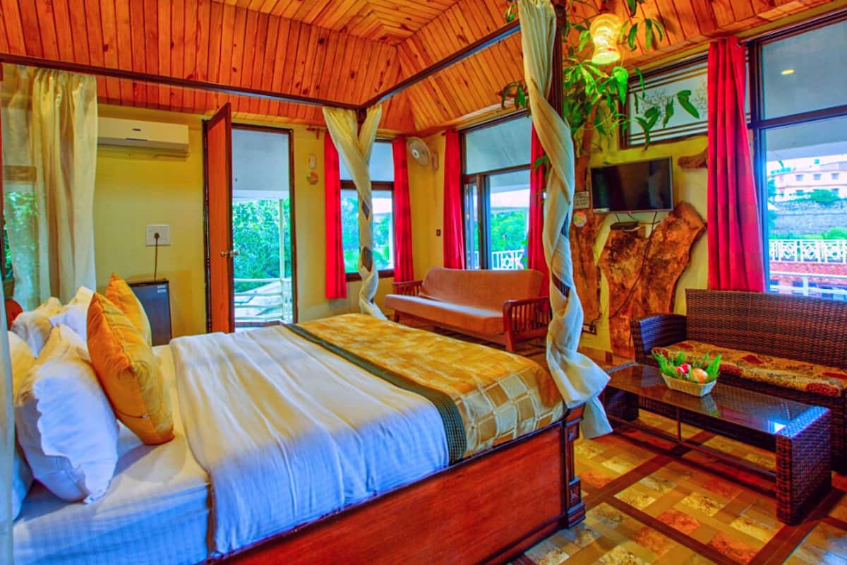 A room with a bed, a table with fruit, a chair, and a view of greenery outside.