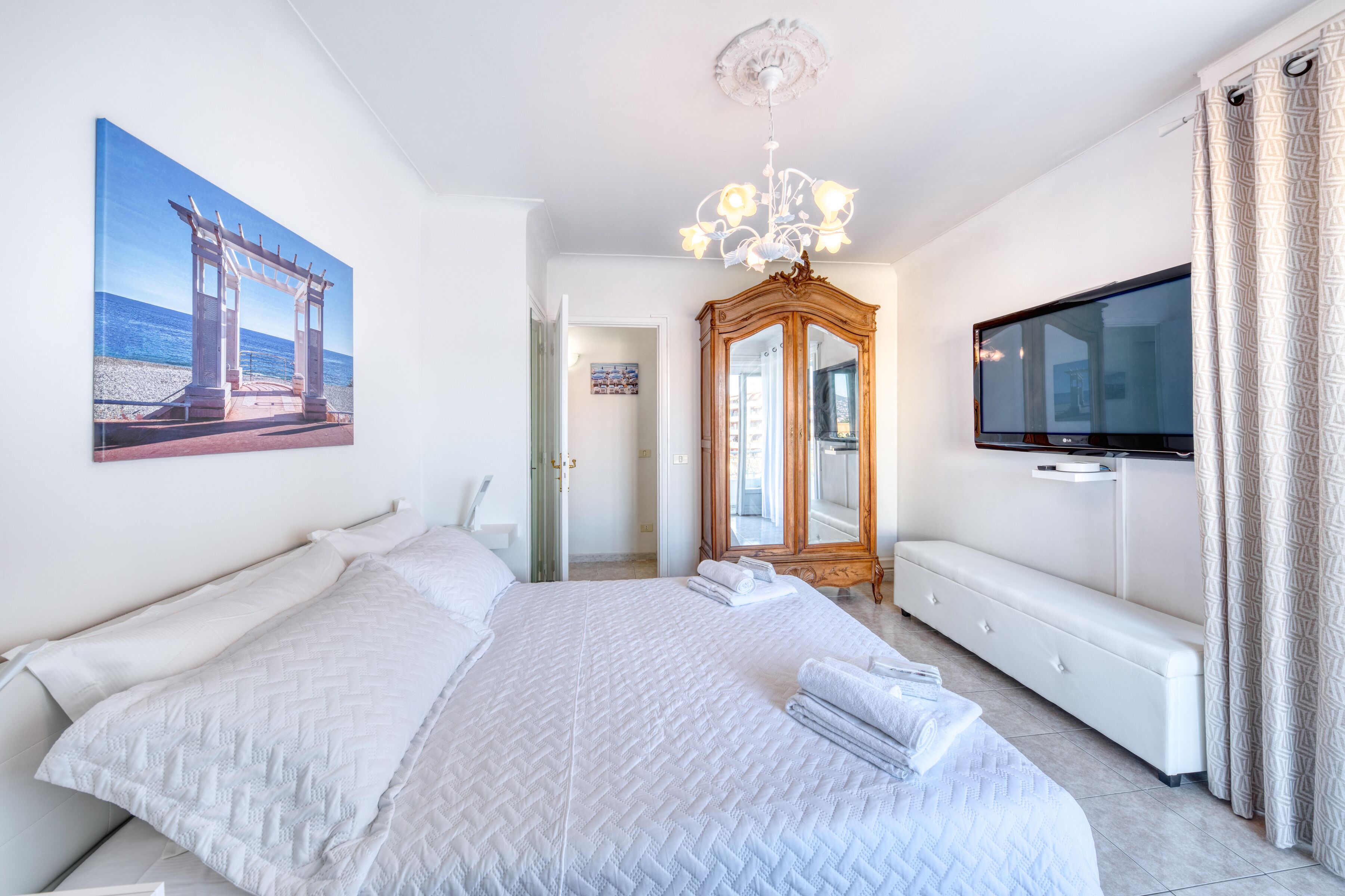 Une chambre spacieuse avec un grand lit, une télévision, une armoire et un tableau représentant une scène de plage.