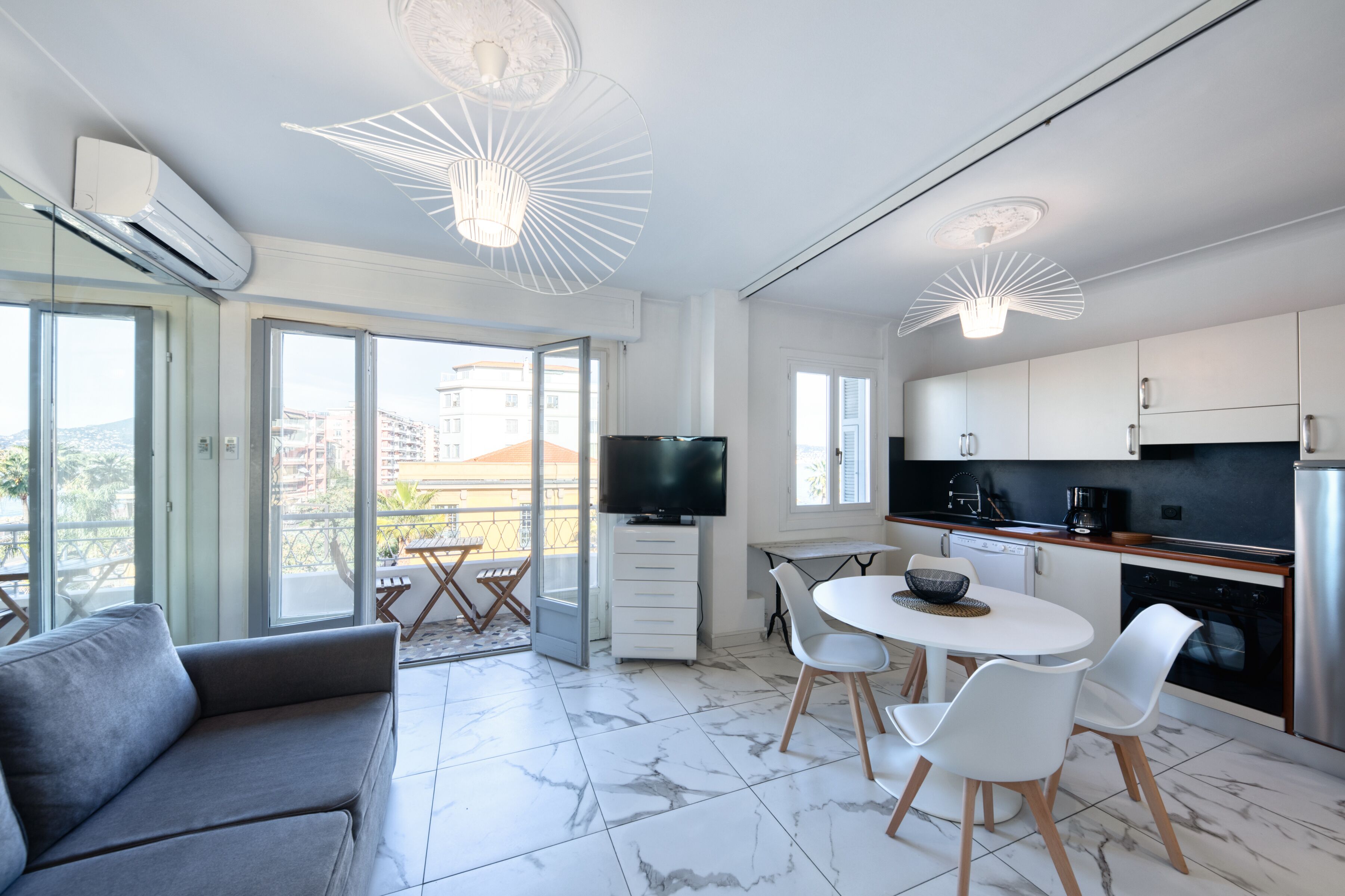A modern apartment with a living area, dining space, and kitchen. It features a large window, a flat-screen TV, and a balcony.