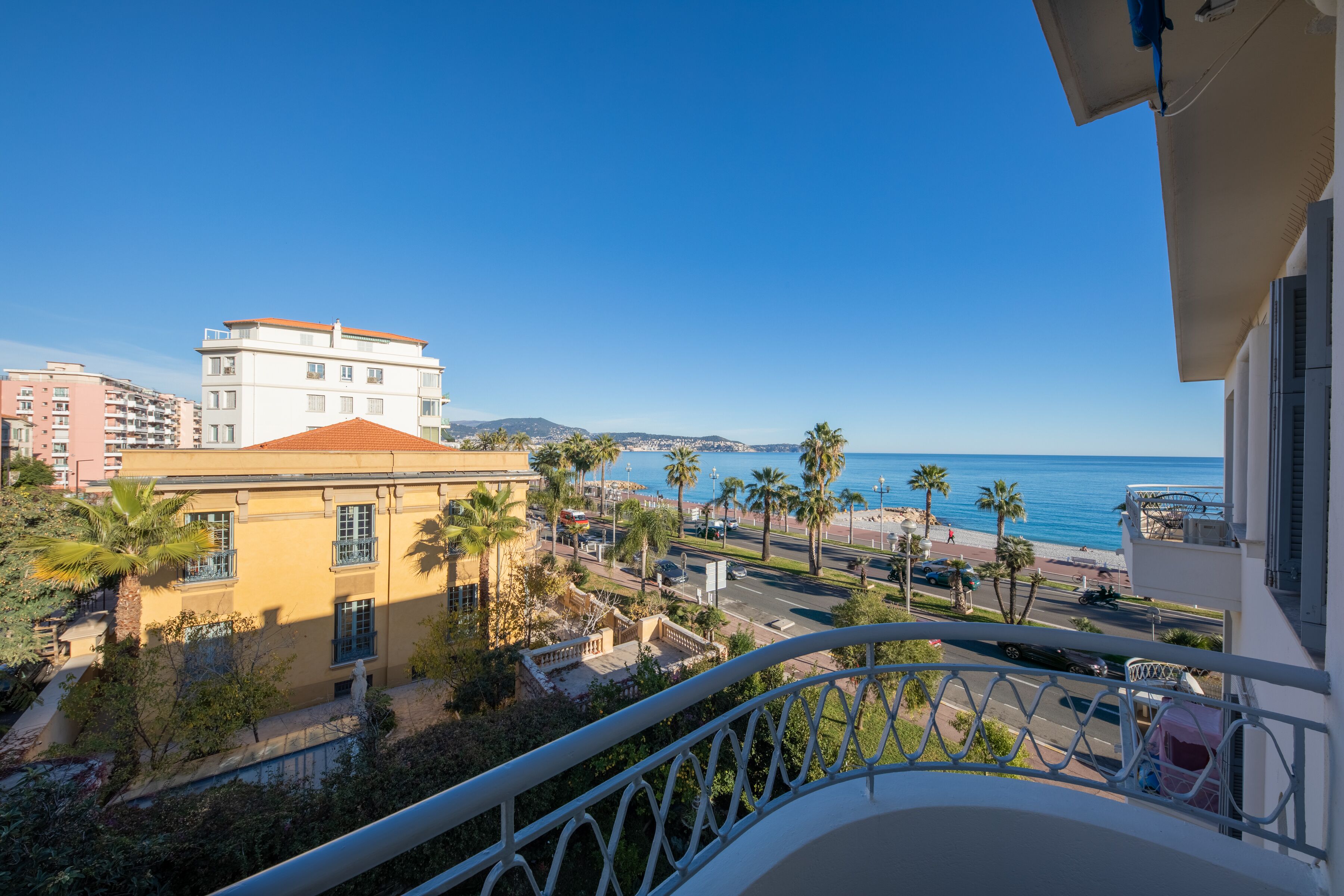 A balcony with a view of a beach, palm trees, and buildings.