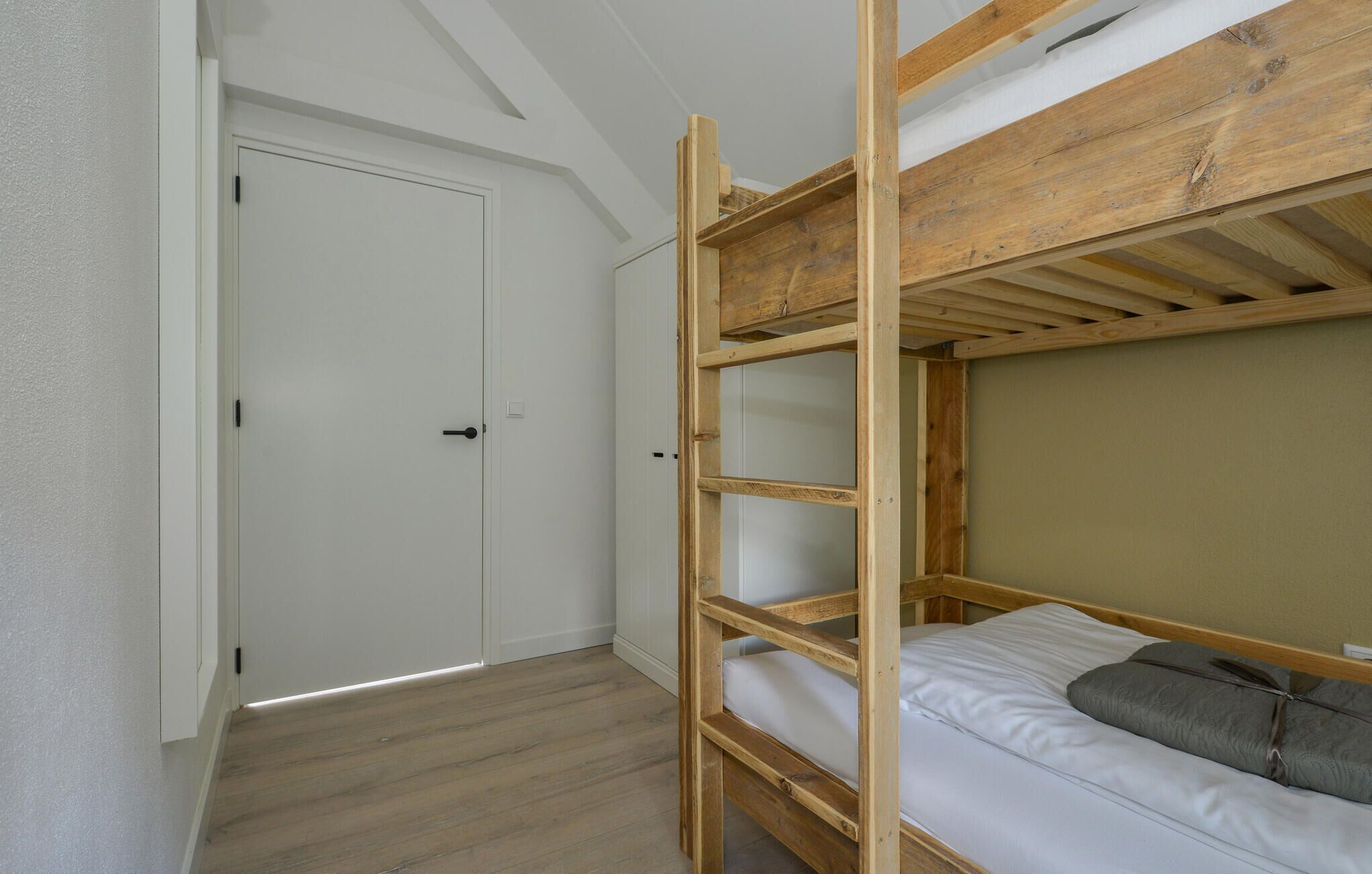 Un lit superposé avec une structure en bois et du linge de lit blanc, une porte blanche et un plancher en bois.