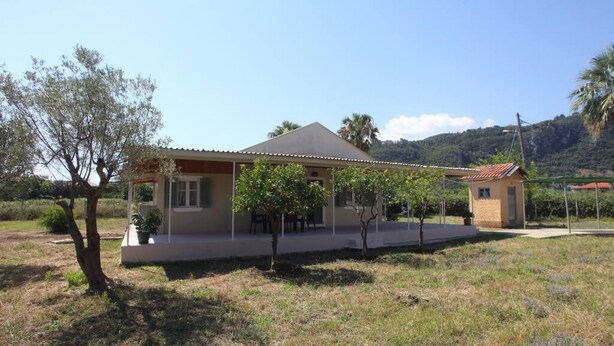 A single-story house with a covered patio, surrounded by trees and a grassy area. - Olga Home Agios Ioannis Lefkada - Lefkada BnB (Lefkada)