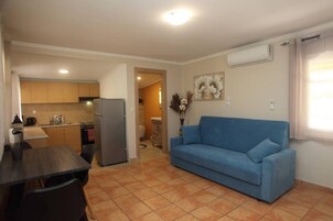 Un espacio habitable compacto con kitchenette, un sofá azul y una zona de comedor.