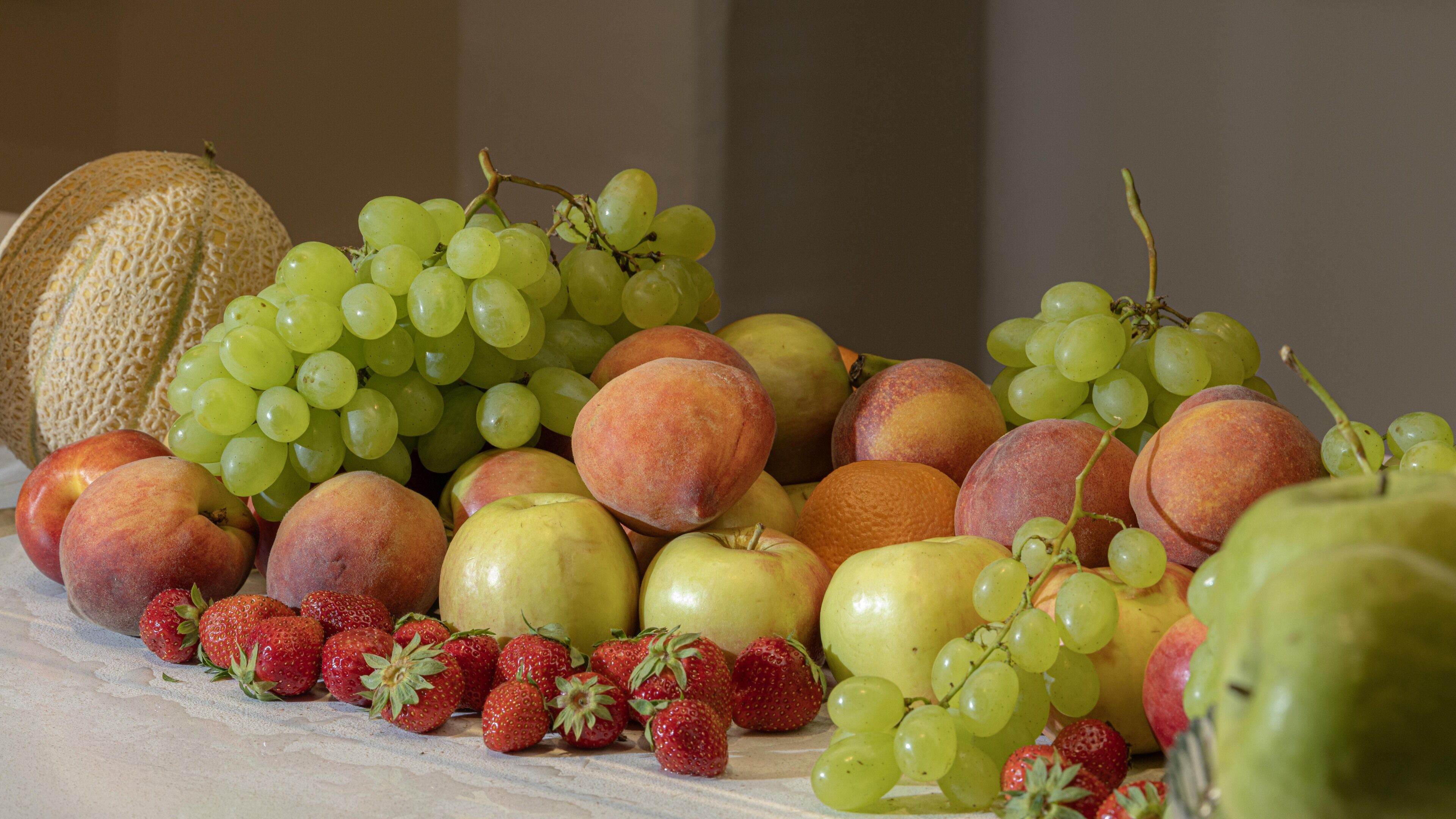 A variety of fruits including grapes, peaches, apples, and strawberries arranged on a marble surface.