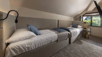 A modern bedroom with two beds, a built-in heater, and a window with a view of trees.