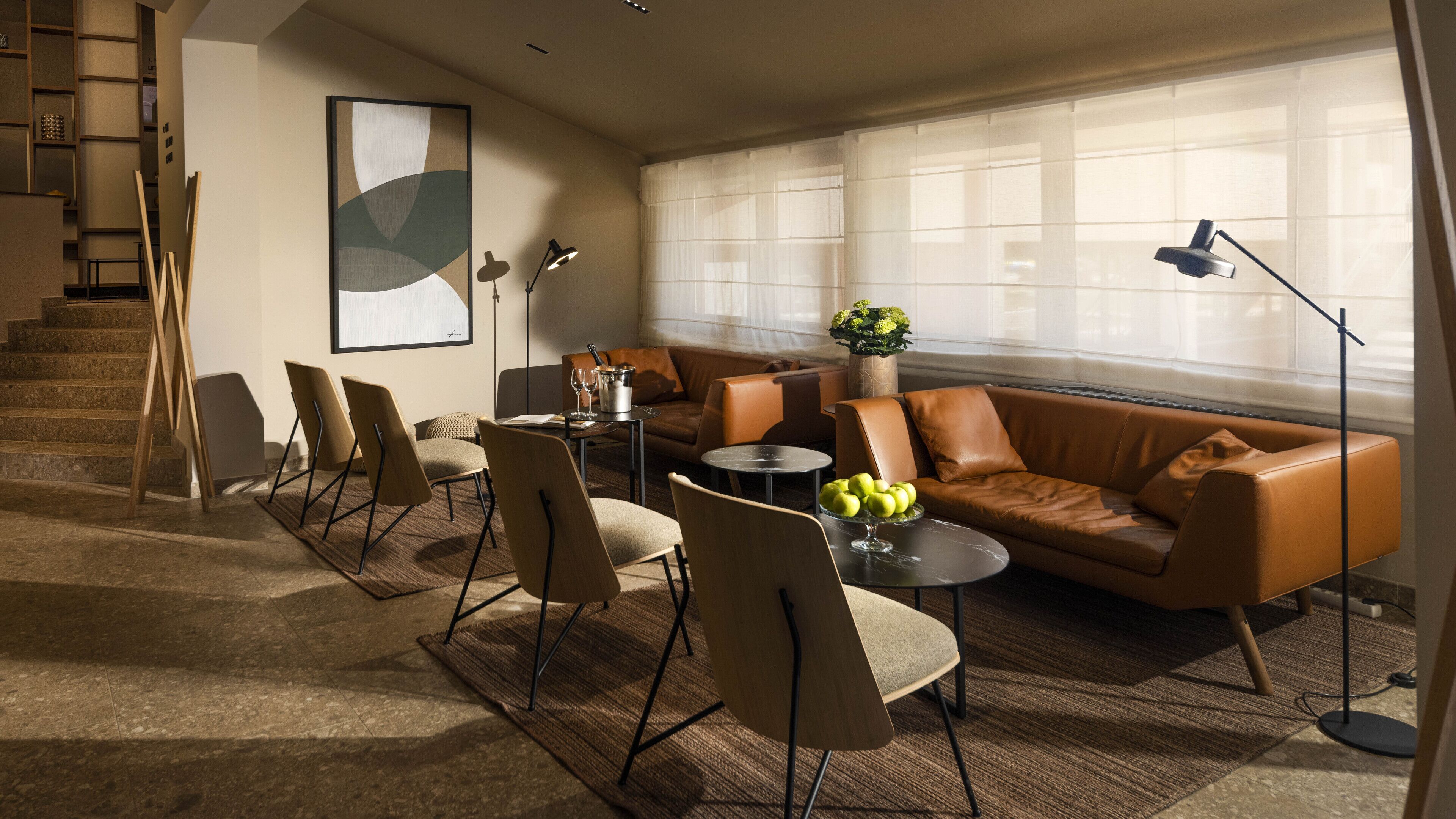 A modern living room with a brown leather sofa, a dining table with chairs, and a large window with sheer curtains.
