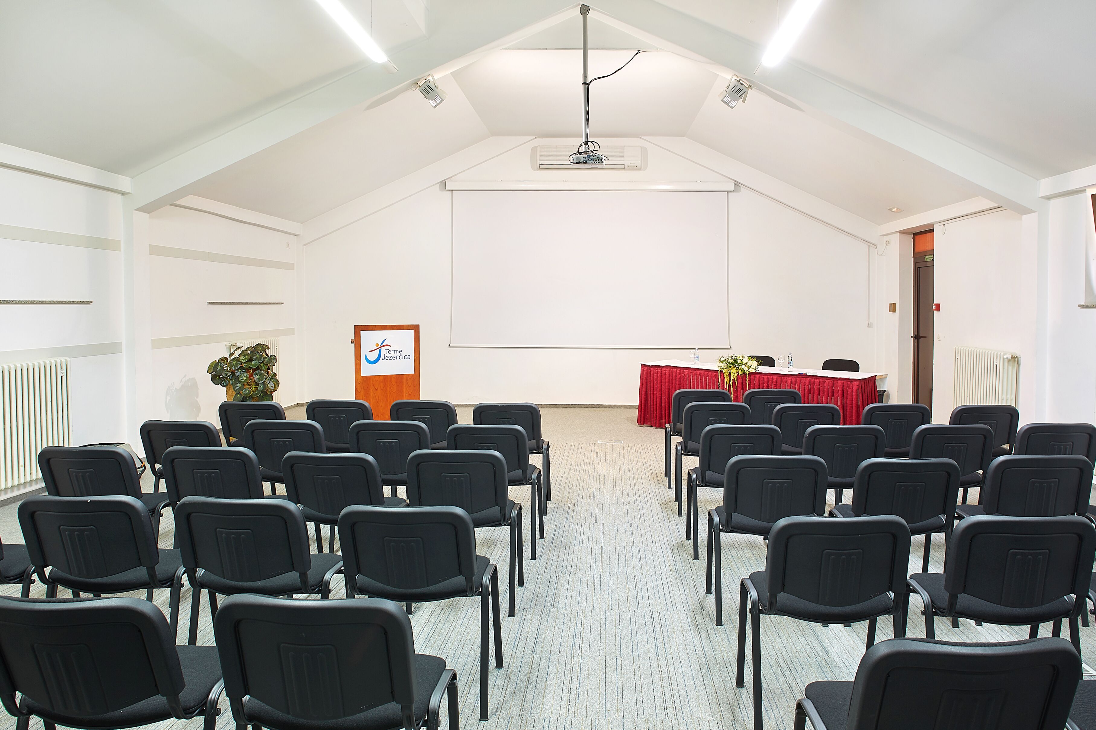 A conference room with rows of chairs, a podium, and a projector screen.