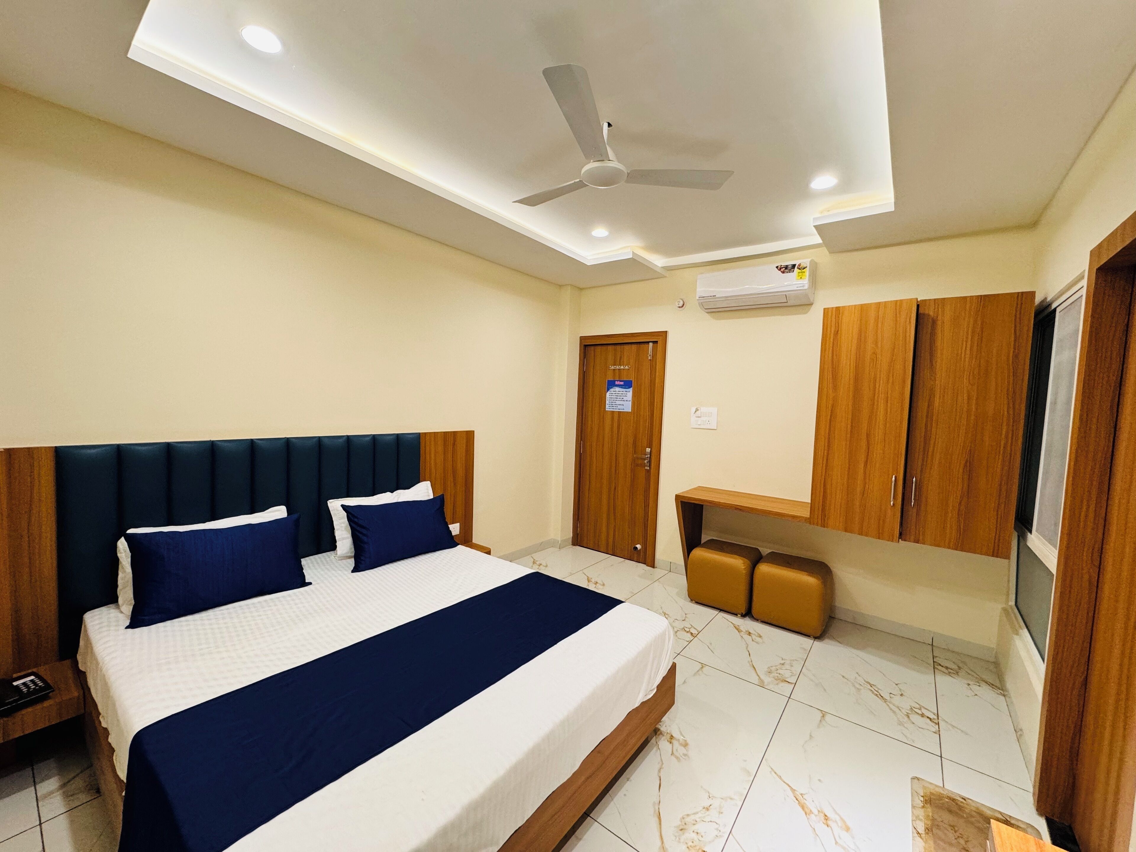 Une chambre d’hôtel avec un lit, un ventilateur de plafond, une armoire et une petite table.
