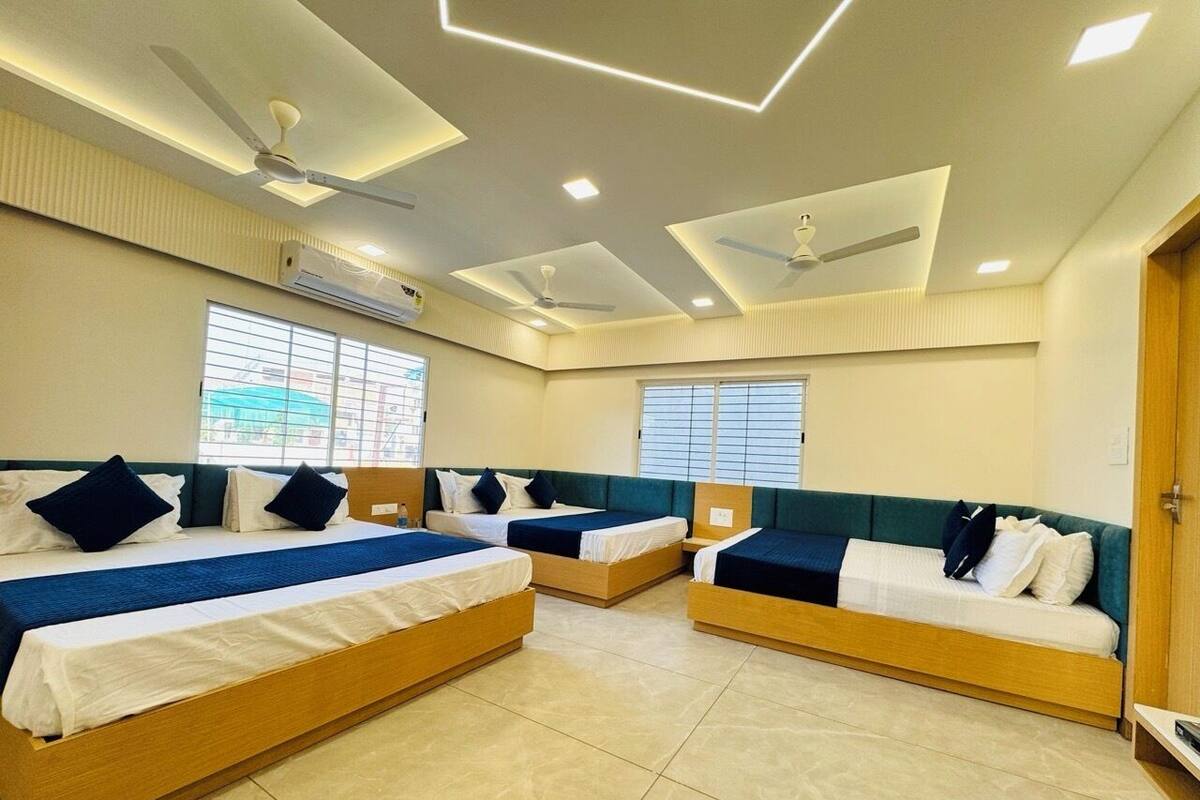 Habitación de hotel con tres camas individuales, ventilador de techo y una ventana grande con persianas.