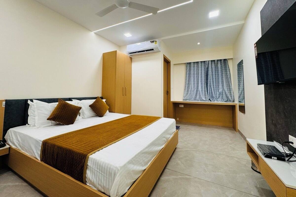 Una habitación de hotel moderna con una cama grande, muebles de madera, un aire acondicionado, un ventilador de techo y una ventana con cortinas.