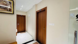 Un pasillo con puertas de madera numeradas 101 y 102, suelo de baldosas blancas y un cuadro en la pared.