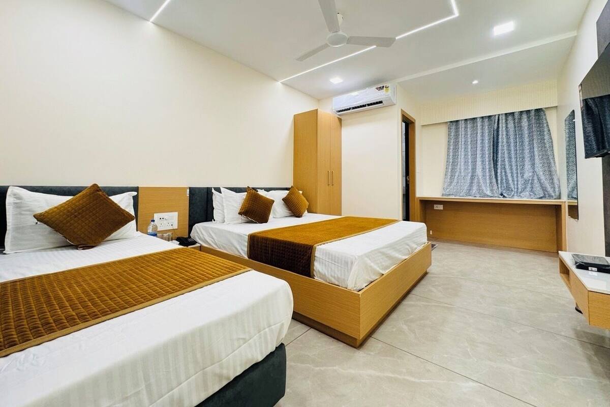 Habitación de hotel con dos camas, ventilador de techo y ventana con cortinas.