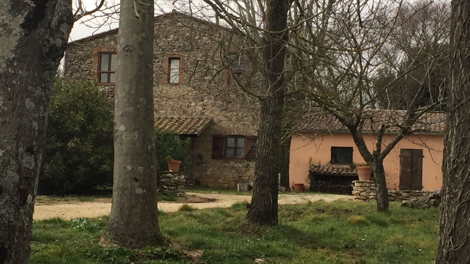 A rustic stone house with a tiled roof, surrounded by trees and a grassy area.
