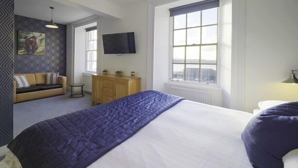 Quarto com cama grande, sofá, TV e janela com vista.