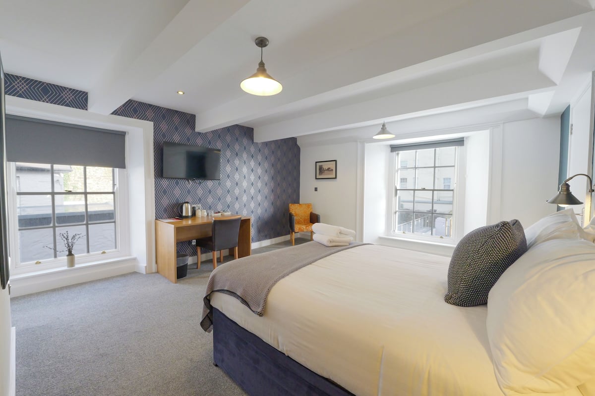 Una habitación de hotel moderna con una cama grande, un escritorio y un televisor montado en la pared.