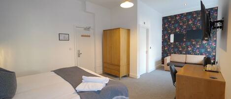 A hotel room with a bed, a wooden wardrobe, a desk, and a sofa.
