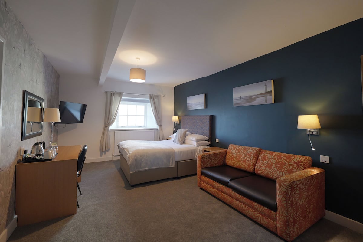 Una habitación de hotel con cama, escritorio, sillón, sofá y televisor fijado a la pared.